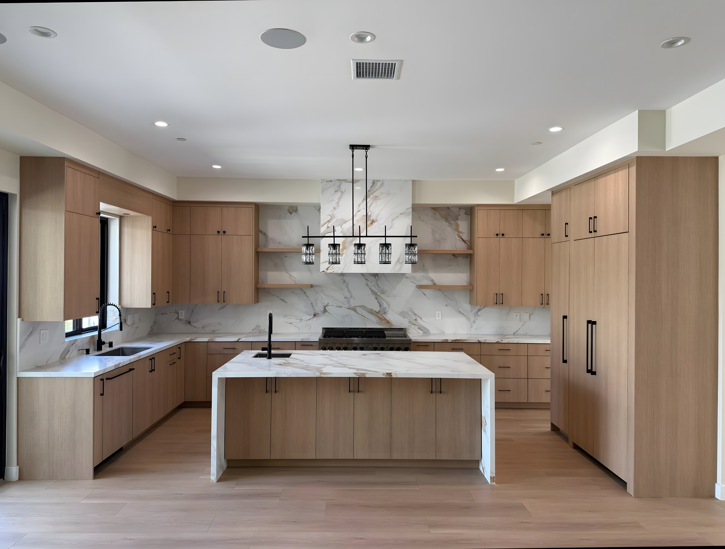Symmetric high-end kitchen: warm white-oak cabinets, calacatta marble feature wall, integrated appliances, modern linear pendant chandelier, light hardwood floor.