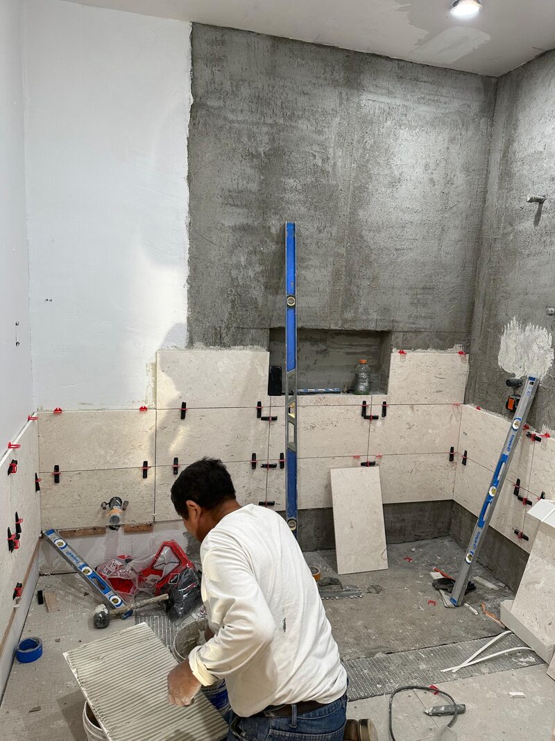 Emner Mendoza on his knees applying mortar, mid-tile install.