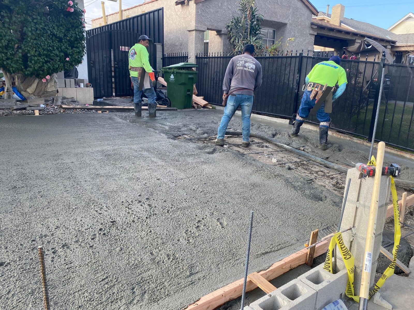 Crew pouring concrete on a residential driveway, brick piers staged at the perimeter.